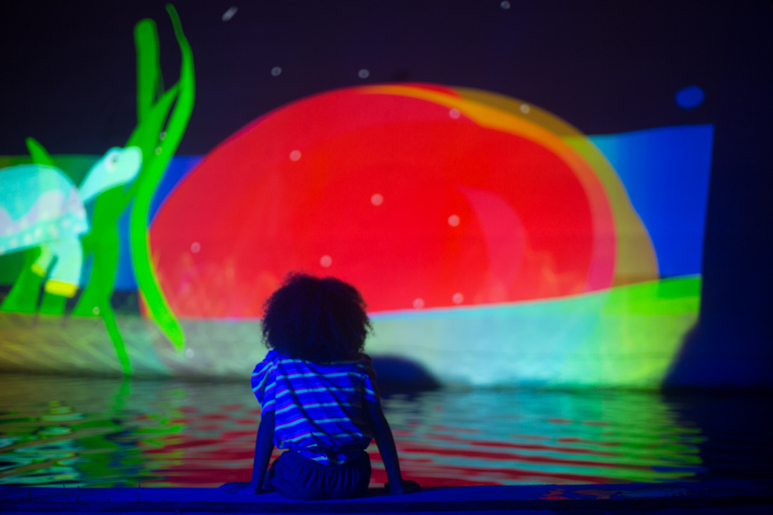 A child sitting by the lake and watching the projections over a surface.